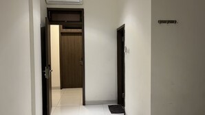 A hallway with a wooden door, a black mat at the entrance, and a wall-mounted air conditioning unit. - Good Day Inn (Jakarta)