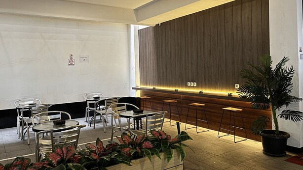 A modern reception area with a wooden reception desk, metal chairs, and potted plants. - Good Day Inn (Jakarta)