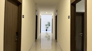 A hallway with wooden doors numbered 104 and 103, leading to a bright room with a potted plant. - Good Day Inn (Jakarta)