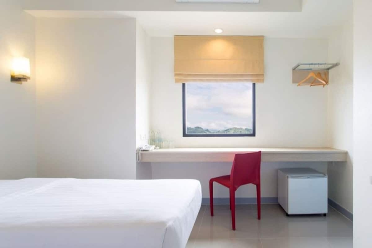 Une chambre d’hôtel comprenant un lit, un bureau avec une chaise, un petit réfrigérateur, une fenêtre avec vue et un luminaire fixé au mur.
