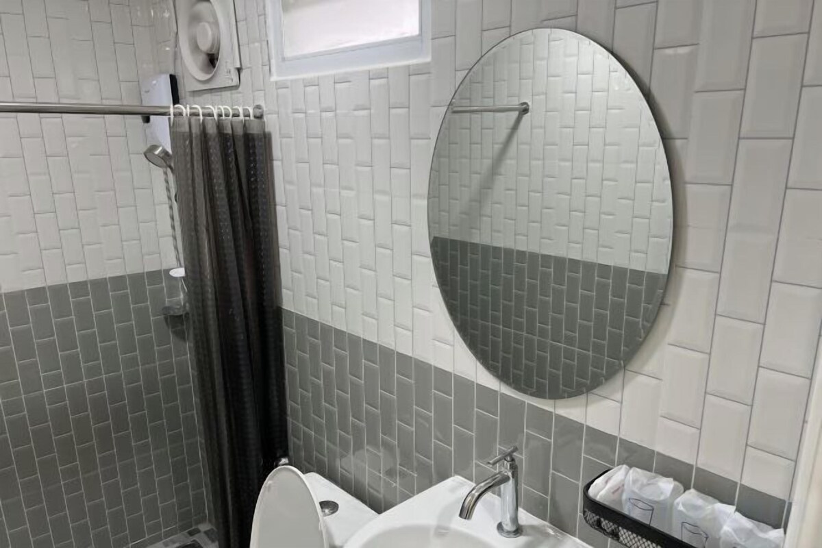 Une salle de bain équipée d’une douche, de toilettes, d’un lavabo et d’un miroir rond fixé au mur.