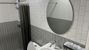 Ein Badezimmer mit Dusche, Toilette, Waschbecken und einem runden Spiegel.