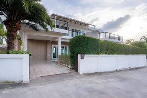 A modern two-story house with a balcony, a driveway, and a well-maintained garden. - Platinum Pool Villa (Sattahip)
