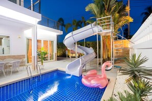Piscina com escorrega, boia em formato de flamingo rosa e escada que leva a uma varanda.