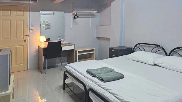 A bedroom with a bed, a desk, a chair, a wardrobe, and a small table.