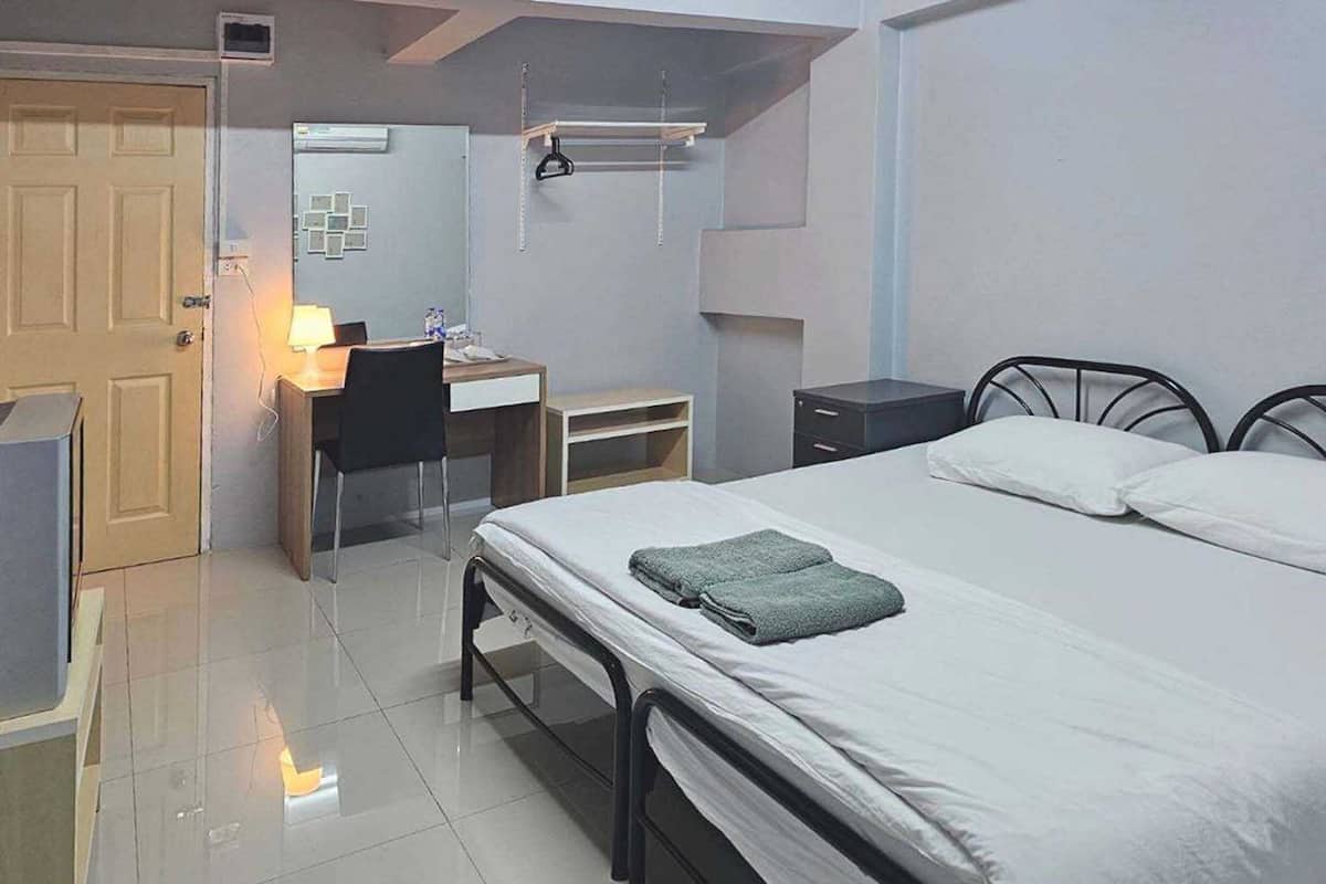 A bedroom with a bed, a desk, a chair, a wardrobe, and a small table.