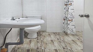 A bathroom with a white sink, toilet, and shower curtain with a floral pattern. The floor has a wood-like tile design.
