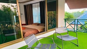 A balcony with a bed, two chairs, and a glass door leading to a room. - Siriniran Homestay (Sattahip)