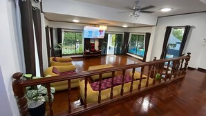 A spacious living area with a wooden staircase, large windows, and a ceiling fan. - Siriniran Homestay (Sattahip)