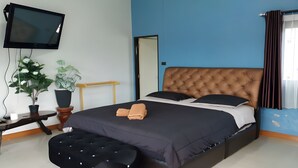 A bedroom with a large bed, a flat-screen TV mounted on the wall, a potted plant, and a wooden side table. - Siriniran Homestay (Sattahip)