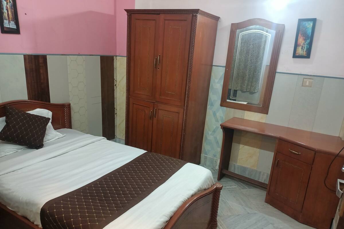 A neatly arranged bedroom with a bed, wooden wardrobe, a mirror, and a desk.