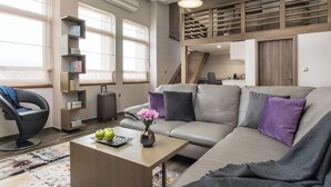 A modern living room with a sofa, a coffee table with apples and flowers, a bookshelf, and a staircase leading to an upper level. - Sevtopolis Apartments (Kazanlak)