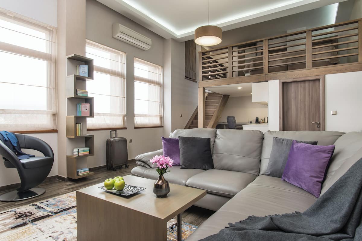 A modern living room with a sofa, a coffee table with apples and flowers, a bookshelf, and a staircase leading to an upper level.
