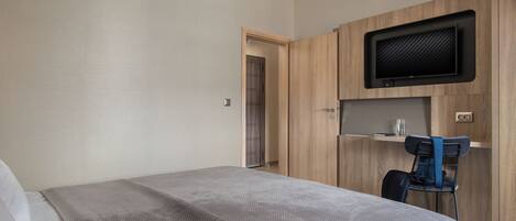 A bedroom with a bed, a desk, and a television mounted on the wall.