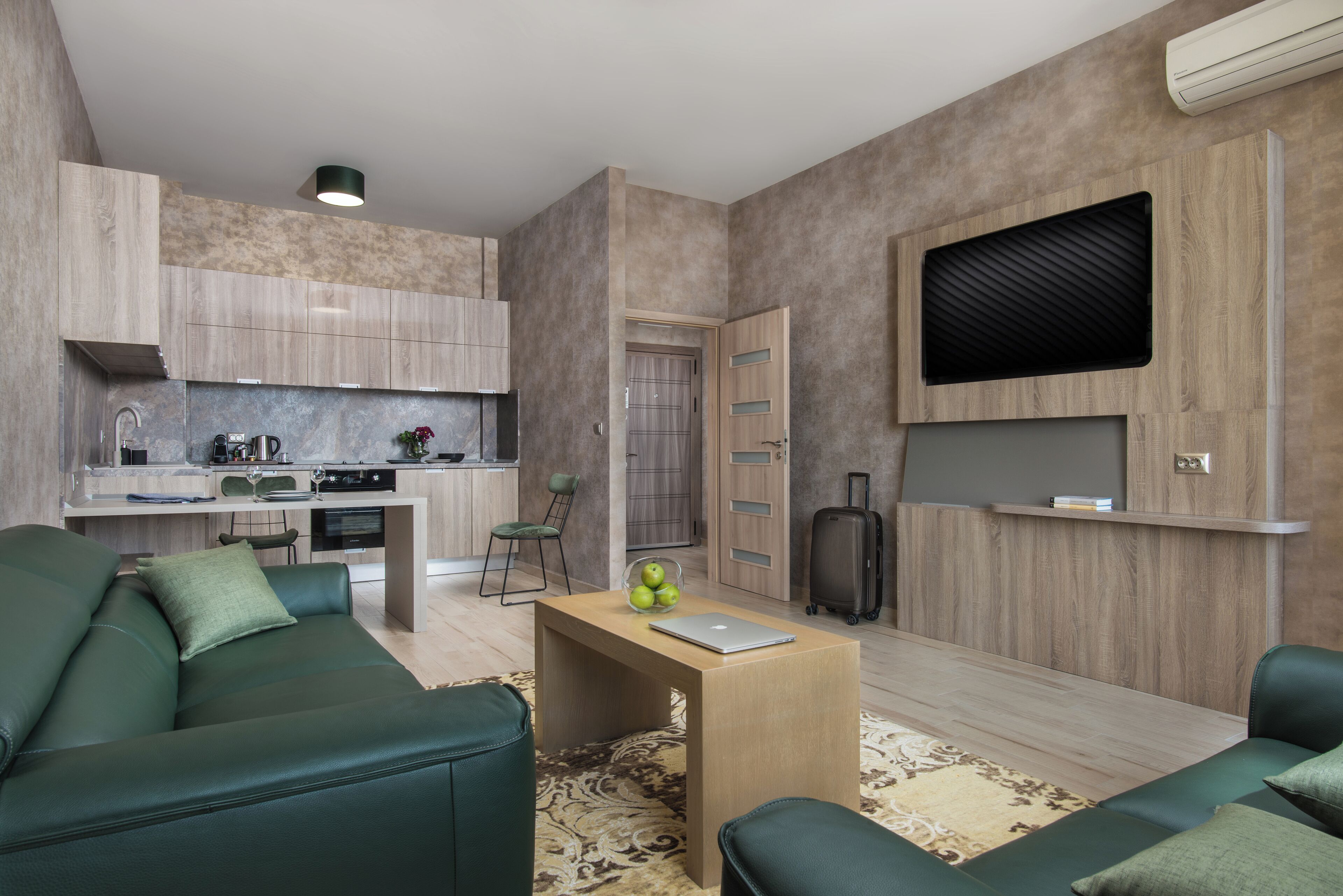 Un salon moderne avec un canapé vert, une table basse en bois et un coin cuisine à l’arrière-plan.