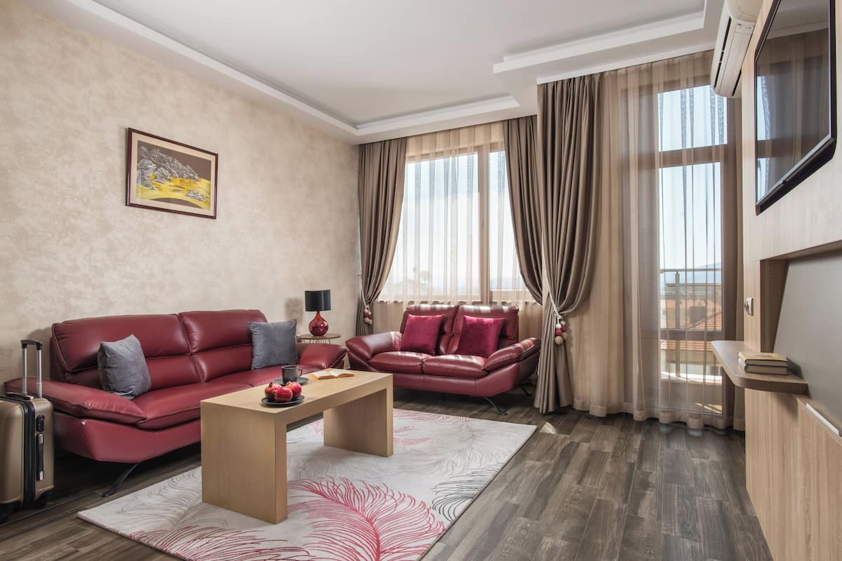 A modern living room with a red leather sofa, a wooden coffee table, and a large window with curtains.