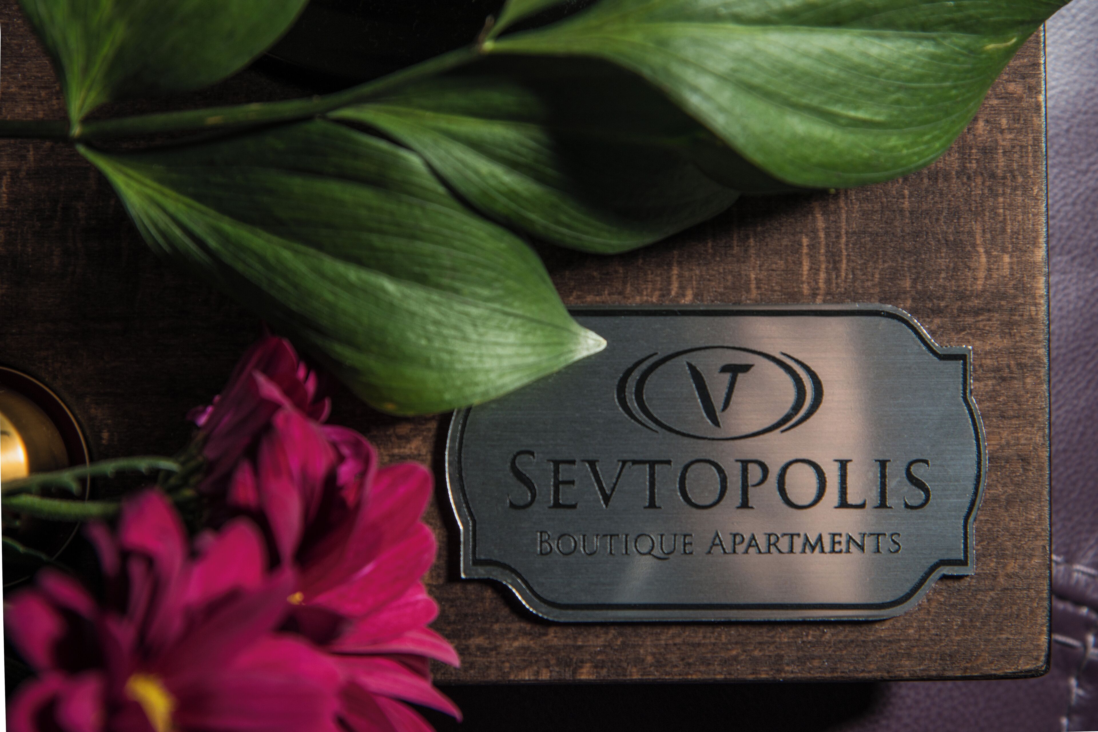 Een metalen bord met de tekst 'SEVTOPOLIS BOUTIQUE APARTMENTS' op een houten ondergrond.