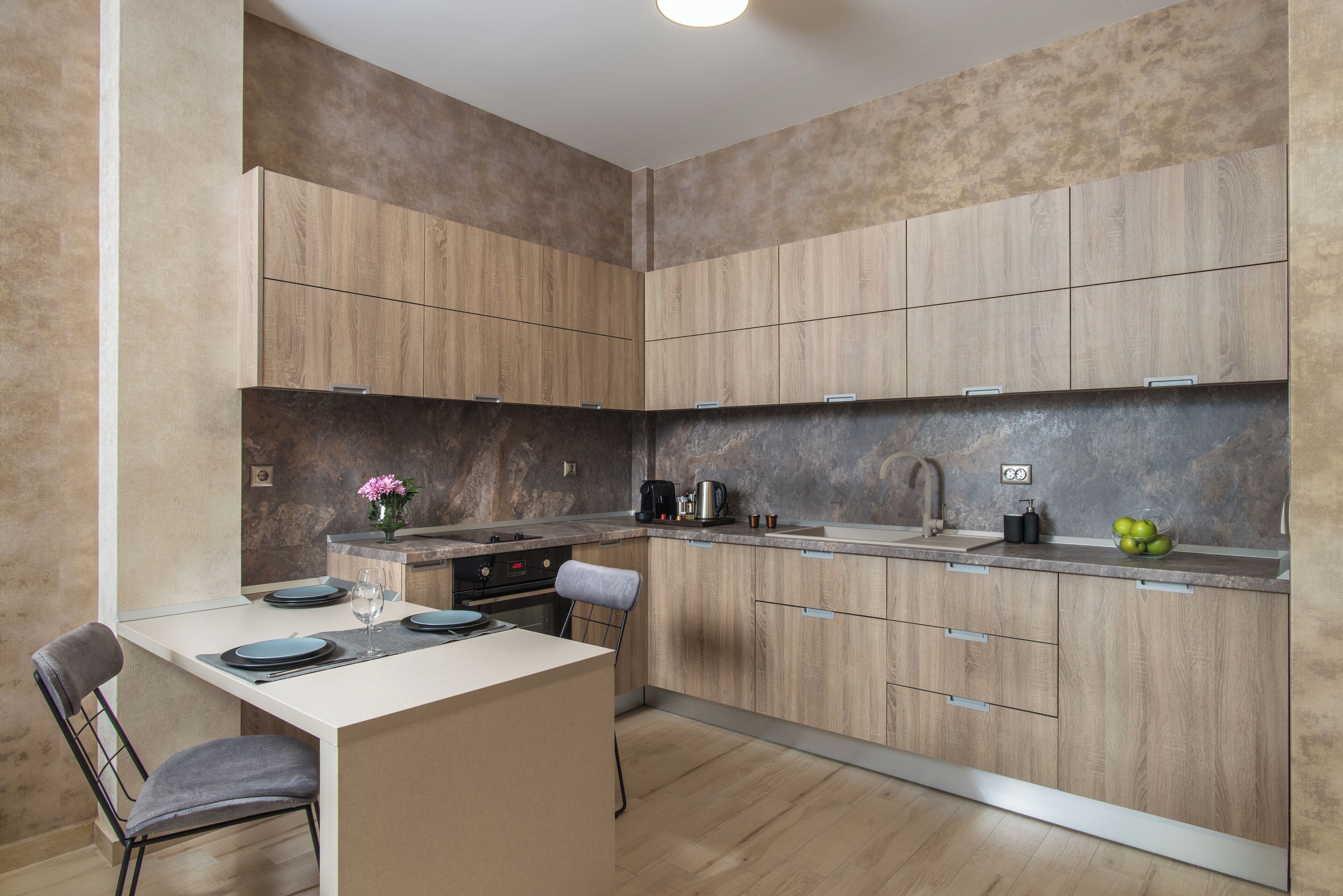 A modern kitchen with wooden cabinets, a dining area with a table and chairs, and a countertop with a coffee maker and fruit bowl.