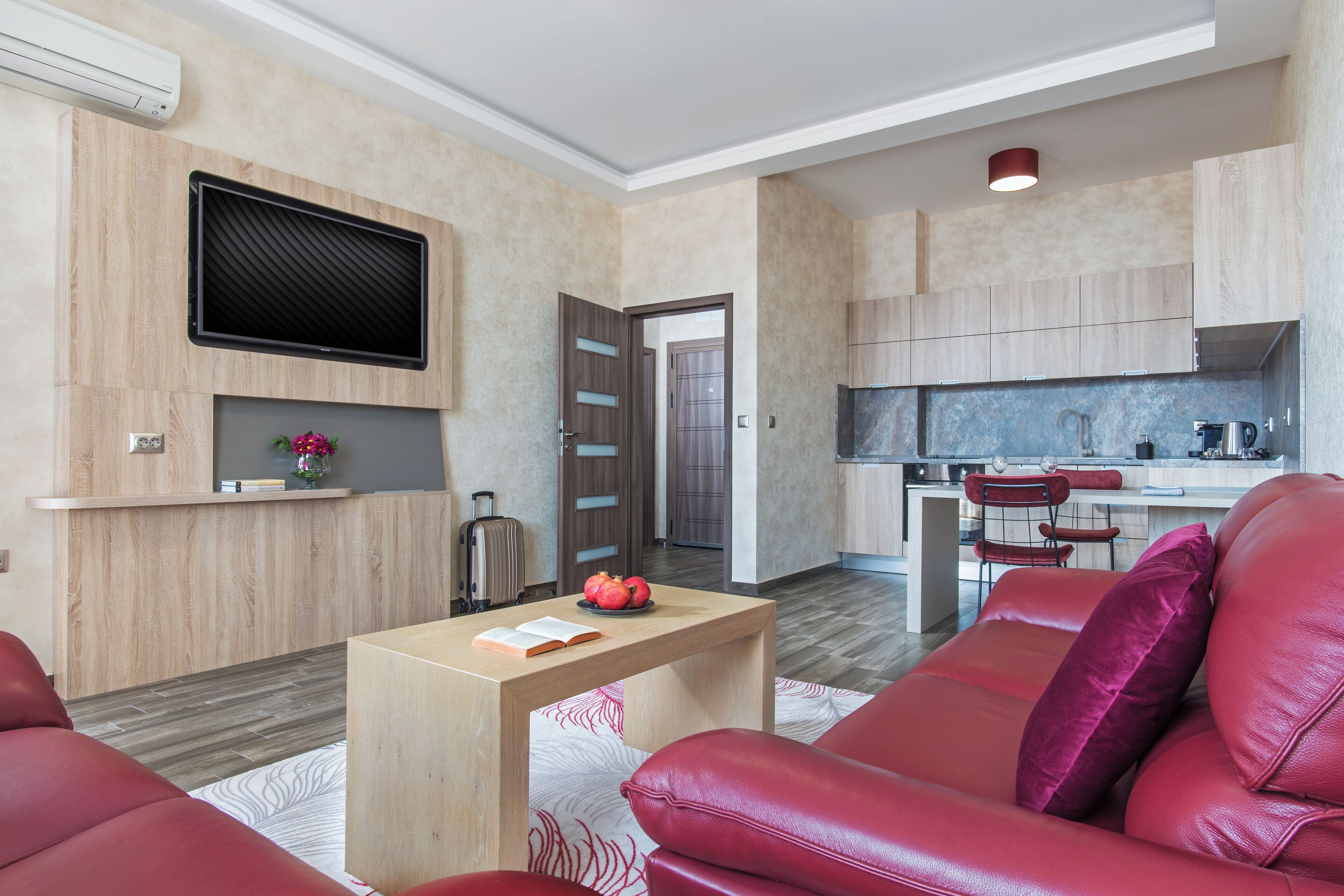 A modern living room with a red leather sofa, a wooden coffee table, and a flat-screen TV mounted on the wall.