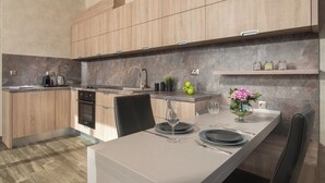 A modern kitchen with wooden cabinets, a built-in oven, and a dining area with a table set for two. - Sevtopolis Apartments (Kazanlak)