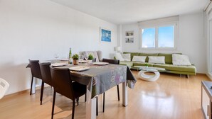 A modern living room with a dining area, featuring a green sofa, a coffee table, and a dining table set for four. - ROYAL MARINE 2 314 Roses (Rosas / Roses)