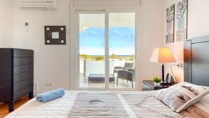A bedroom with a bed, a dresser, a lamp, and a view of a balcony with outdoor furniture. - ROYAL MARINE 2 314 Roses (Rosas / Roses)