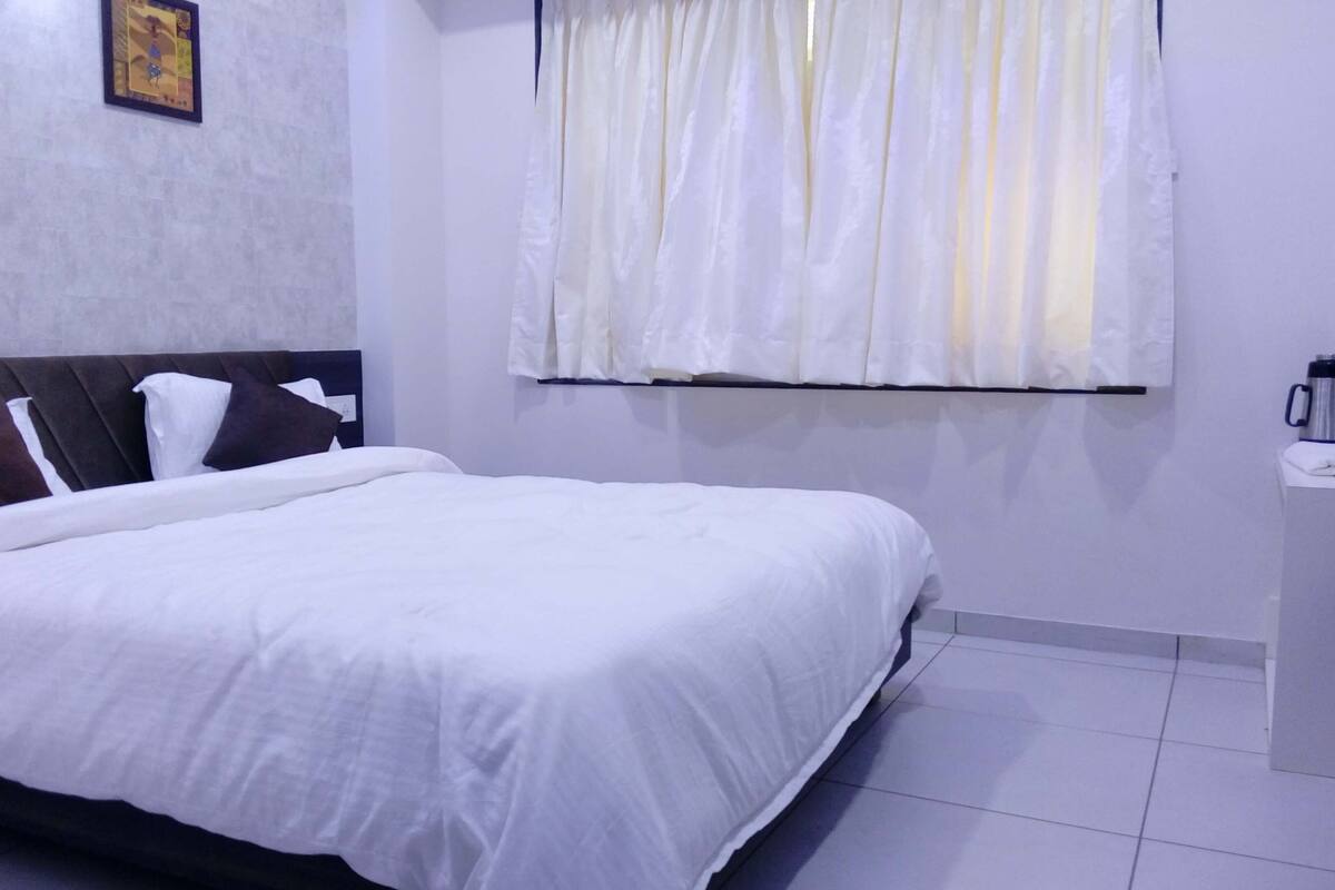 A neatly made bed with white bedding, a headboard, and a bedside table with a coffee maker.