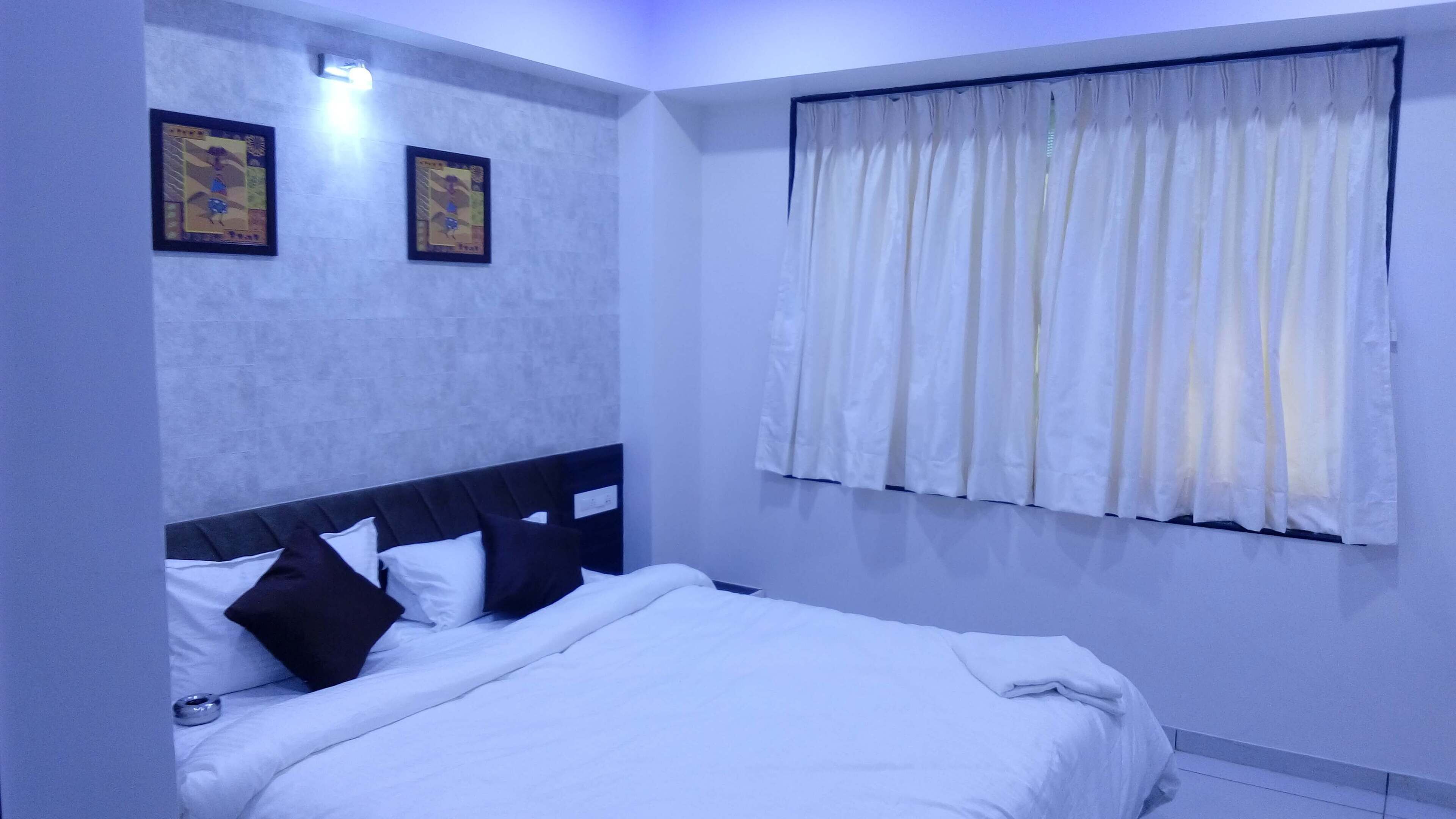 Un dormitorio con una cama, dos cuadros enmarcados en la pared y una ventana con cortinas.