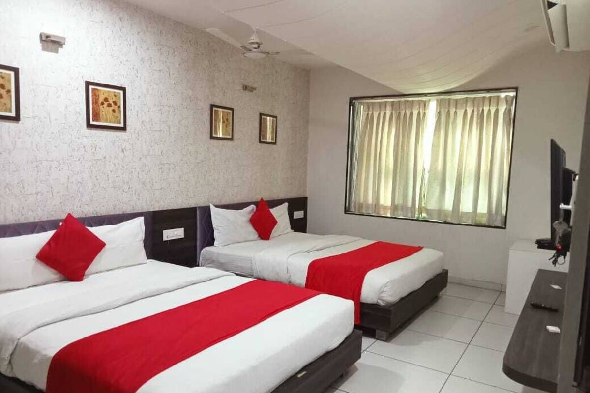 A hotel room with two beds, a large window with curtains, a flat-screen TV, and a ceiling fan.