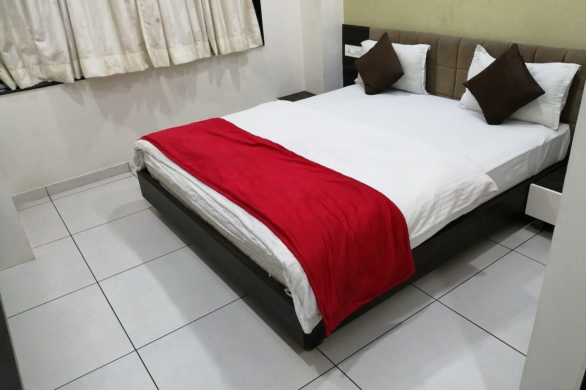 A neatly made bed with a red blanket, white bedding, and brown pillows.