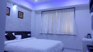Un dormitorio con cama, ventana con cortinas y una lámpara fijada a la pared.