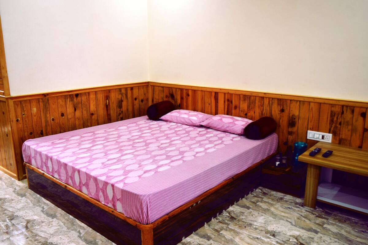 A single bed with a patterned bedspread, a wooden headboard, a nightstand with a lamp, and a power outlet.
