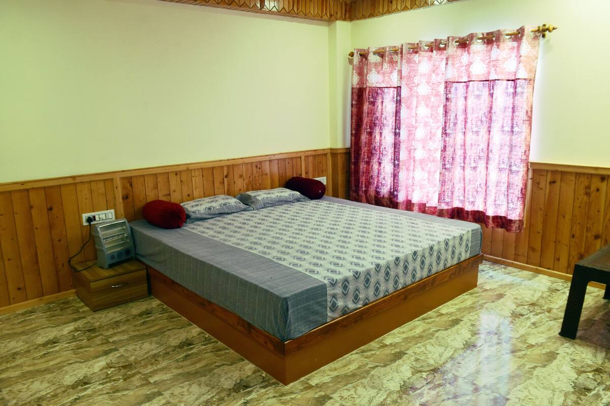 A wooden-paneled bedroom with a bed, a heater, and a window with curtains.