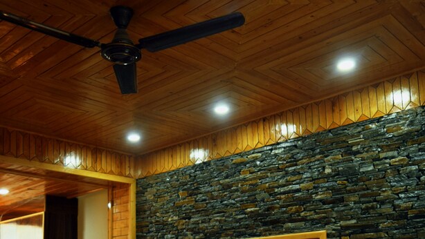 Una habitación con techo de madera, pared de piedra y un televisor fijado a la pared.