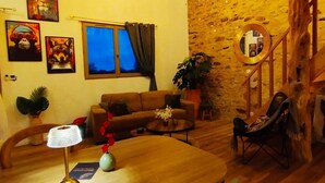 A cozy living room with a sofa, coffee table, and a chair. There is a window with curtains, a mirror, and artwork on the walls.