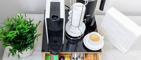 A coffee maker, a coffee pot, a cup of coffee, a plant, and a box of coffee pods.