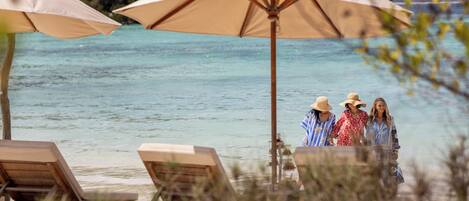 Una playa con sillas de descanso y sombrillas, una vista despejada del océano y un litoral rocoso.