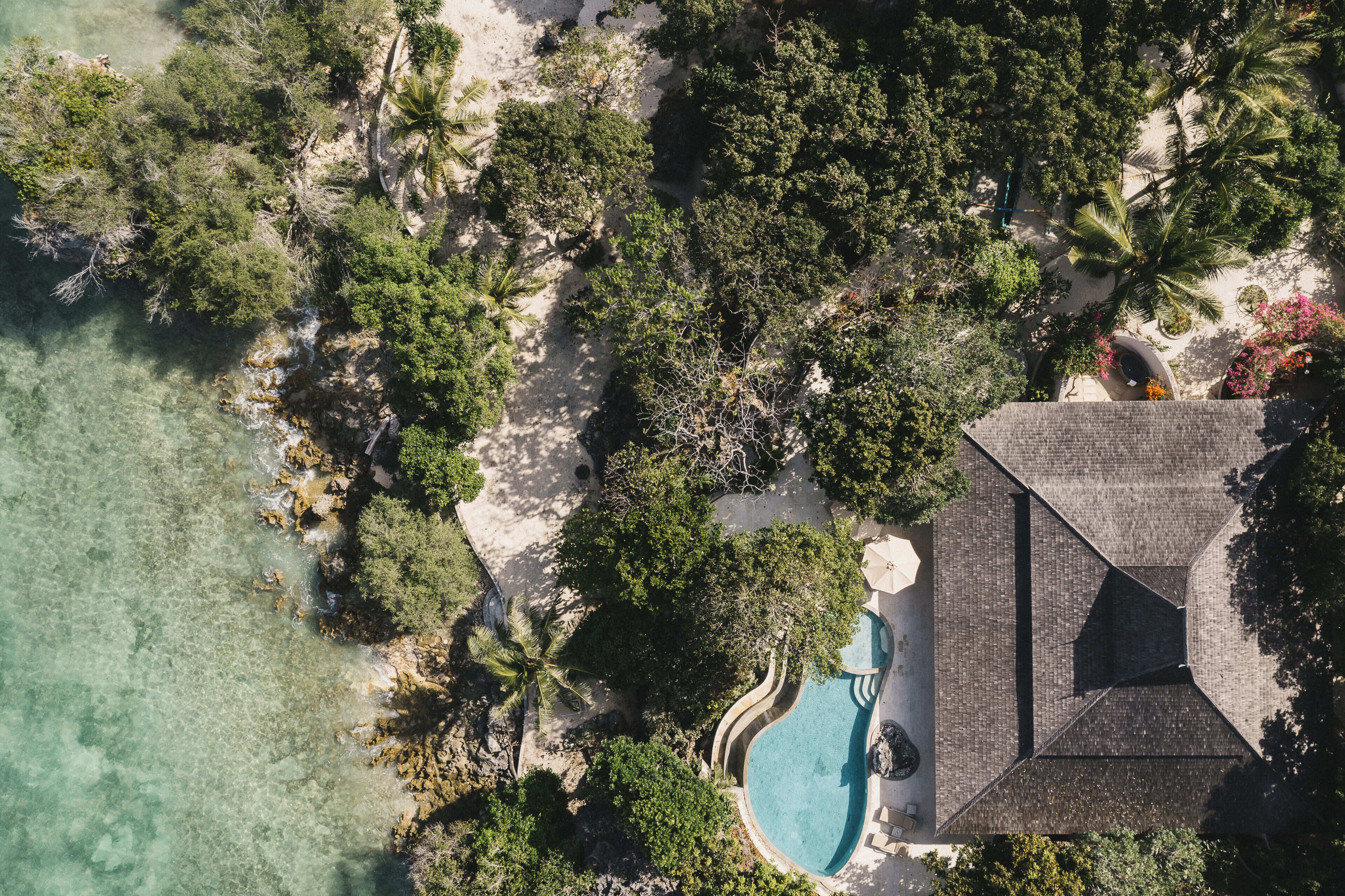 An aerial view of a resort with a swimming pool, palm trees, and a beach.