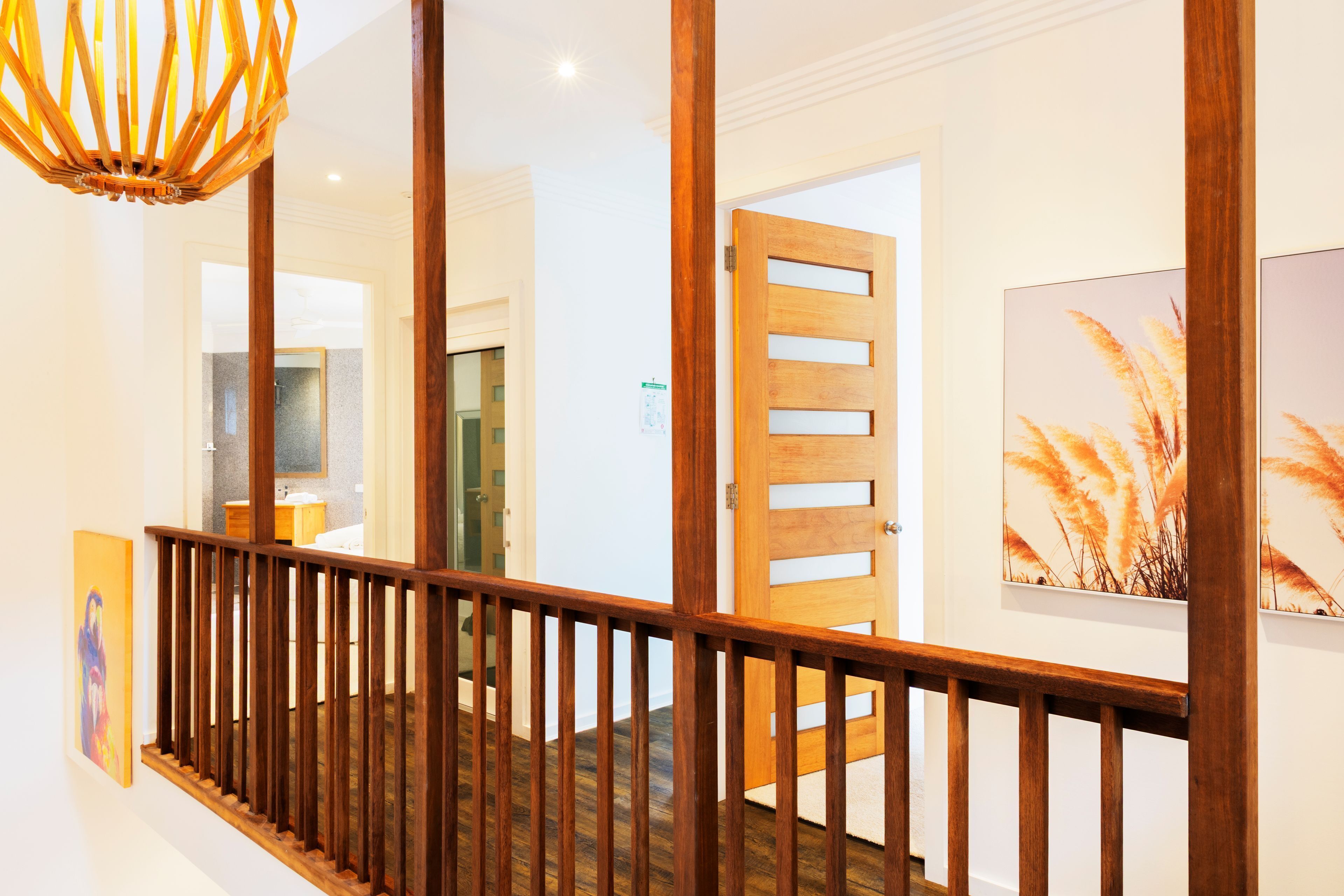 A wooden staircase with a railing, leading to a room with a bathroom and a door with a frosted glass panel.