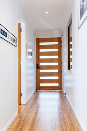 A hallway with a wooden door, a sign indicating direction to the beach, and a framed picture on the wall.