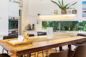 A modern kitchen with a large island, stainless steel appliances, and a view of greenery outside.
