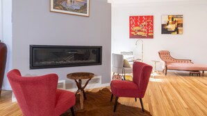 Een woonkamer met een grote flatscreen televisie aan de muur, een houten salontafel en twee rode fauteuils.
