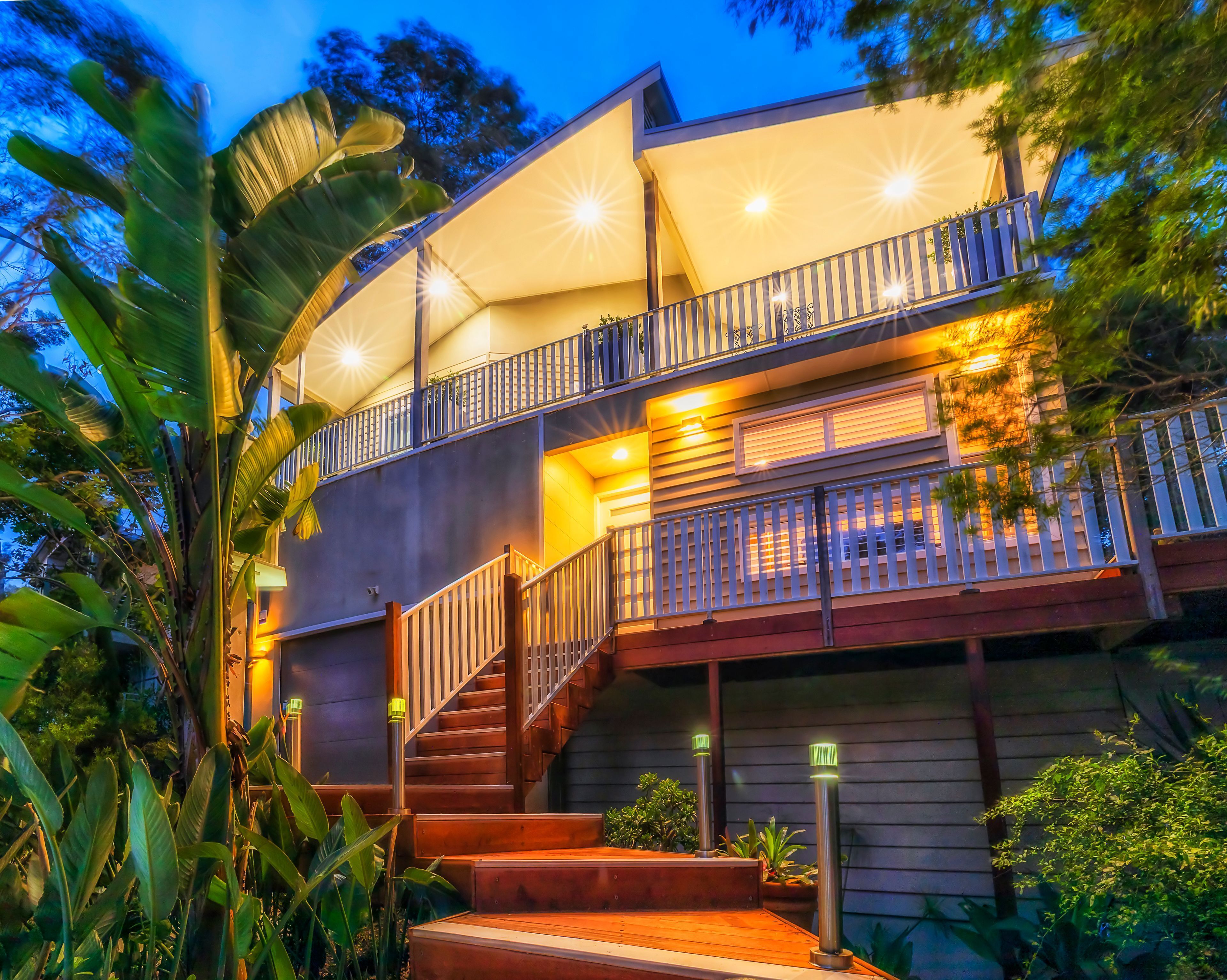 A multi-level residential building with a staircase, outdoor lighting, and lush greenery.