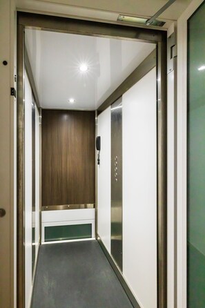 Un pasillo estrecho con pared de paneles de madera, un teléfono y una puerta de ascensor metálica.