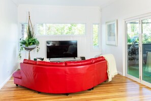 A modern living room with a red leather sofa, a flat-screen TV, and a hanging plant.