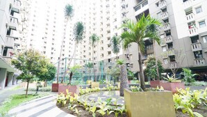 Un immeuble résidentiel doté de nombreux balcons, d’une cour aménagée avec des palmiers et d’un sol pavé à motifs géométriques.