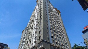 Un immeuble résidentiel de grande hauteur, doté de nombreux balcons, d’une façade sobre et se dressant sur un ciel bleu clair.