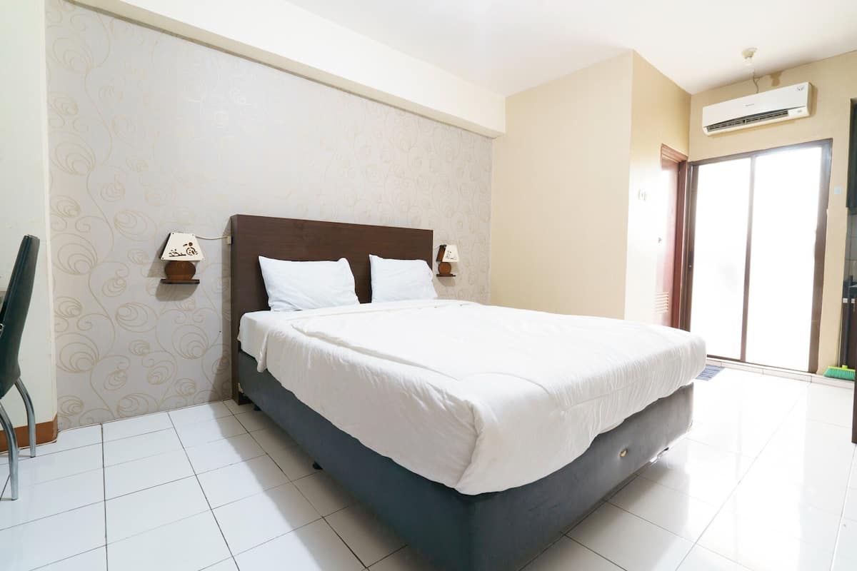 Een hotelkamer met een groot bed, een nachtkastje, een lamp en een raam met uitzicht.