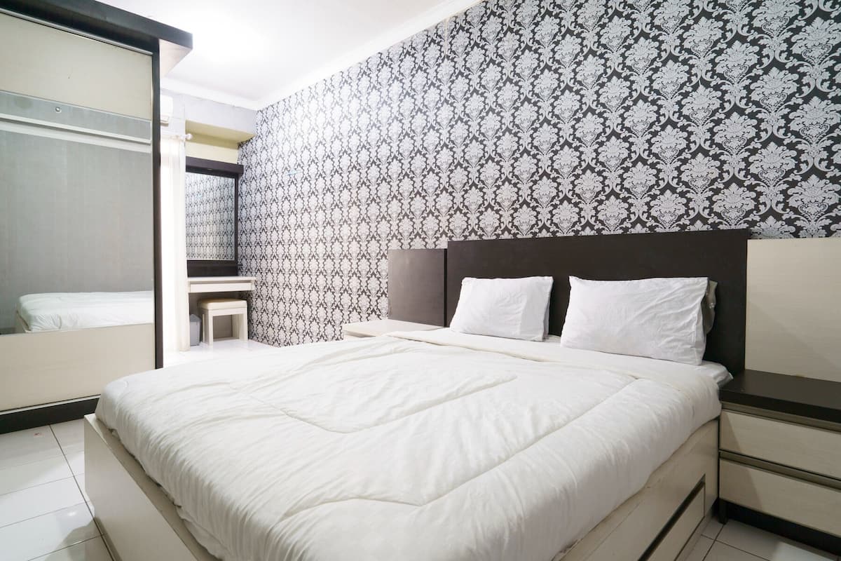 Een slaapkamer met een bed, een nachtkastje, een spiegel en behang met een patroon.