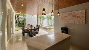 A modern kitchen with a wooden ceiling, pendant lights, a large island, and a dining area with chairs and a table. - Mila's Villa Large 3 bedroom villa in the heart Legian. (Bali)